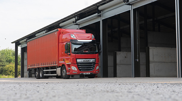 A red lorry sits outside a large warehouse