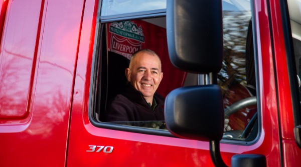 A man smiles from the driver window of a red lorry